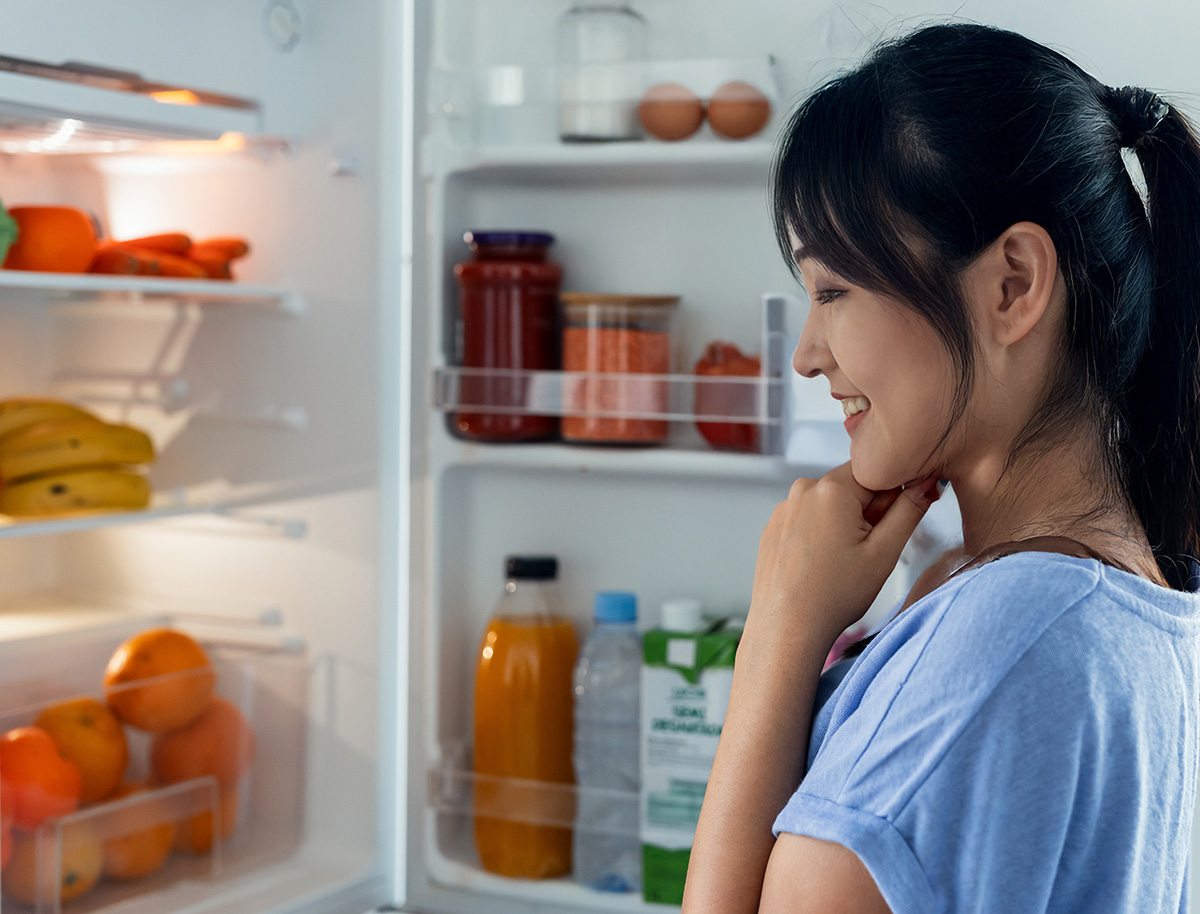 Ragazza asiatica sorridente, guarda all'interno del frigo pieno di cibi sani
